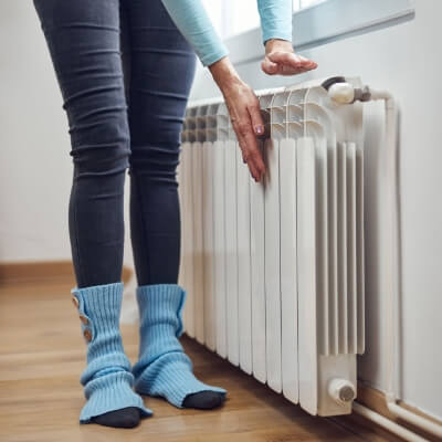 Woman checking the heat coming from the radiator in her home.